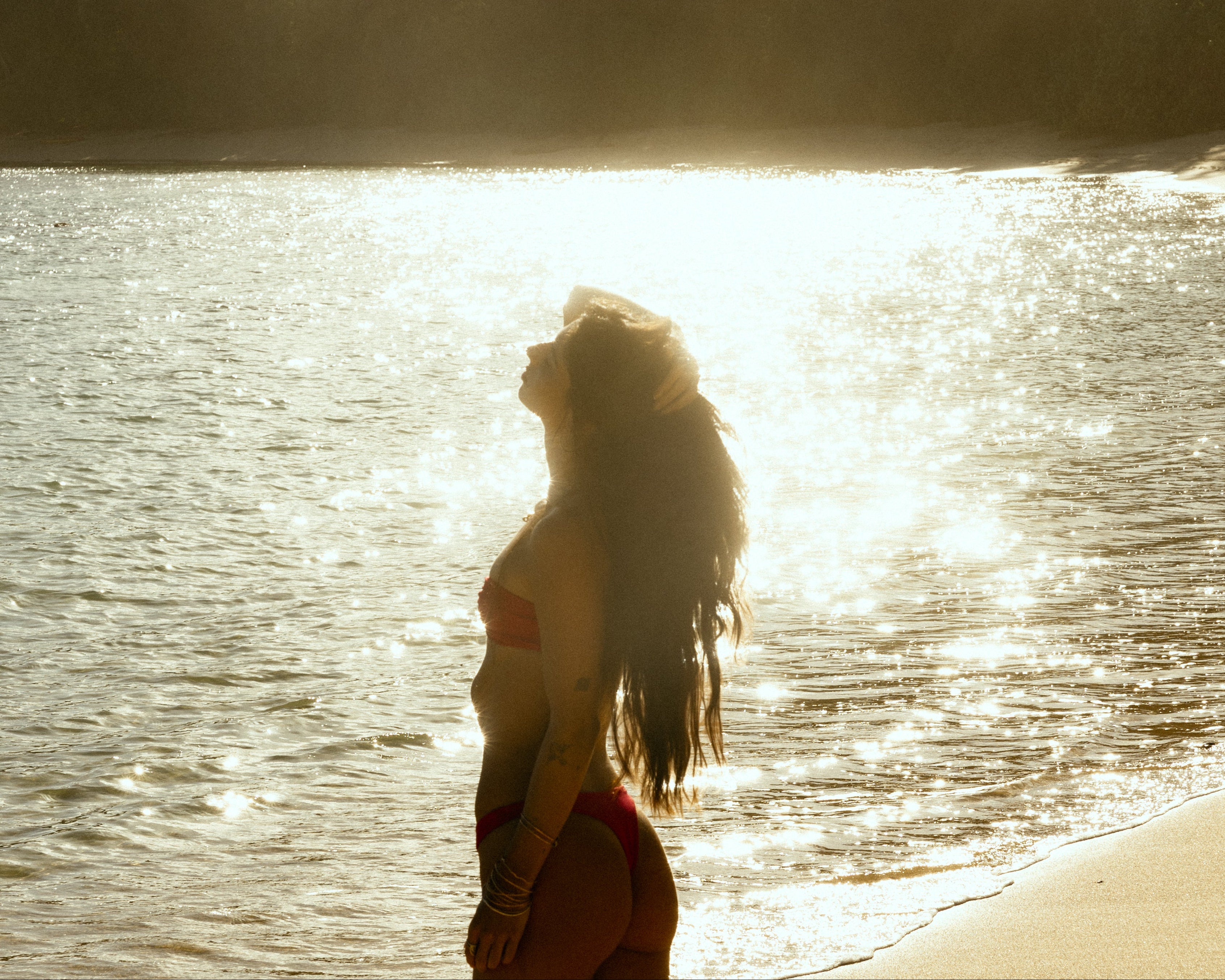 Woman standing by a body of water with sunlight creating a silhouette effect