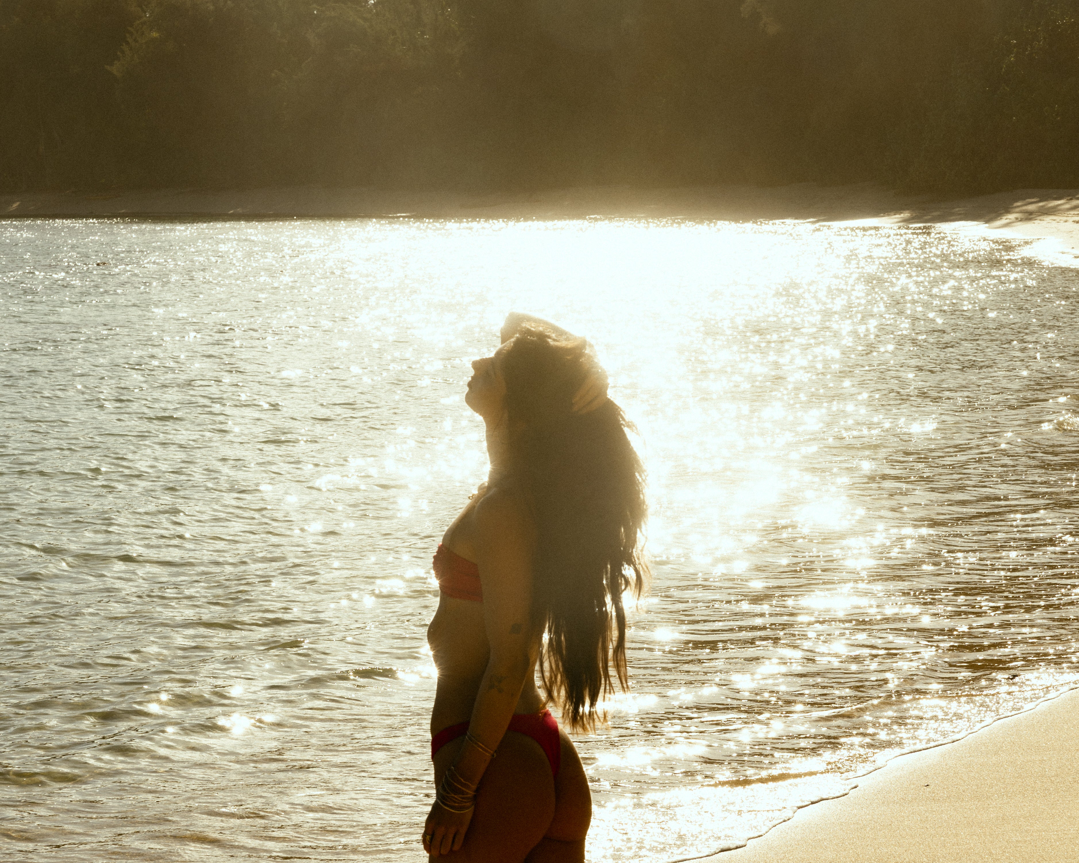 Woman standing by a body of water with sunlight creating a silhouette effect
